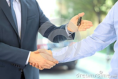 Car salesman handing over the keys for a new car to a young businessman . Handshake between two business people. Focus on a key Stock Photo