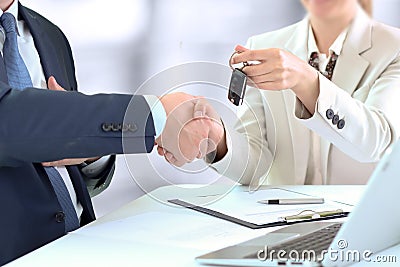 Car saleswoman handing over the keys for a new car to a young businessman . Handshake between two business people Stock Photo