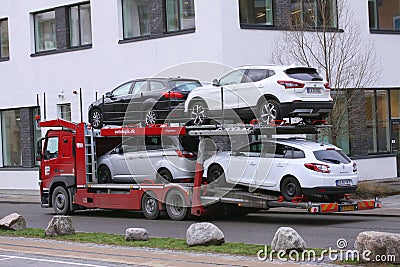 Car shipping auto transport vehicle with cars loaded driving in front of office buildings Editorial Stock Photo