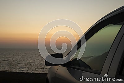 The car is standing over a cliff by the sea. The sunset rays of the sun are reflected in the glass. Pink and orange tones create Stock Photo