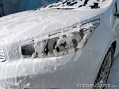 Car wash in foam. Carwash service. White vehicle headlight in soap. Ecology problem in city. Protection and wash auto concept. Stock Photo