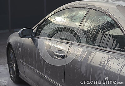 Car wash with soap. Fragment of gray vehicle with active foam. Sunny lighting. Stock Photo