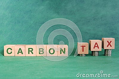 Carbon CO2 emission taxation concept. Carbon tax word in wooden blocks with increasing stack of coins. Stock Photo