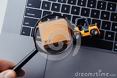 Cardboard box, model of loader and a magnifying glass. Concept of internet commerce, online shopping, trade and turnover Stock Photo