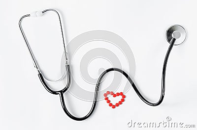 Cardiovascular system. Stethoscope and red pills in a heart shape on white background. Copy space. Stock Photo
