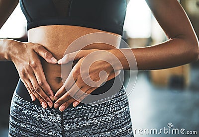 Care enough to keep your core strong. a fit young woman making a heart shaped gesture over her stomach in a gym. Stock Photo