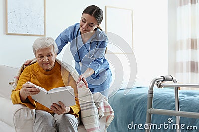 Care worker covering elderly woman with plaid in hospice Stock Photo