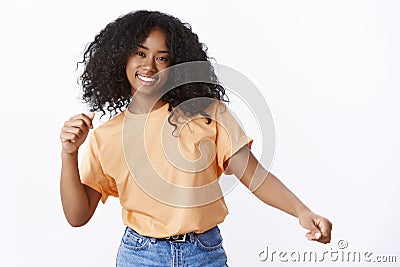 Carefree attractive happy young african-american curly-haired girl wearing spring orange t-shirt dancing waving hands Stock Photo