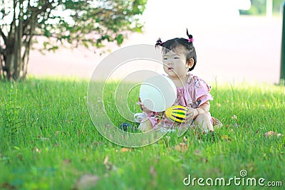 Carefree Chinese baby girl play a ball and balloon on the lawn Stock Photo