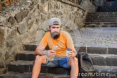 Carefree hipster eat junk food while sit on stairs. Hungry man snack. Junk food. Guy eating hot dog. Man bearded enjoy Stock Photo