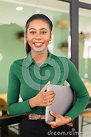 Carefree inspired african-american female employee standing in modern office space and holding laptop, cheerful black Stock Photo