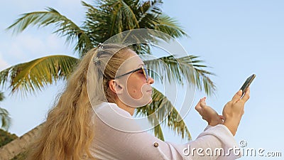 Carefree woman spend her holidays on tropical island near palm tree and coconut cocktail.Smart woman use mobile phone Stock Photo