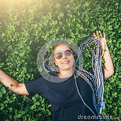 Carefree young happy smiling girl with braided hair lying in clover meadow or green grass, top view Stock Photo