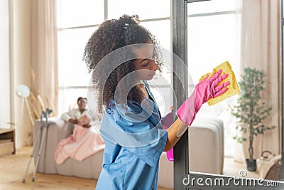 Curly caregiver cleaning the glass door at home of patient Stock Photo