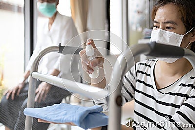 Caregiver in a mask,using spraying alcohol antiseptic,disinfecting spray,cleaning on walking aids,walker for the senior,during Stock Photo