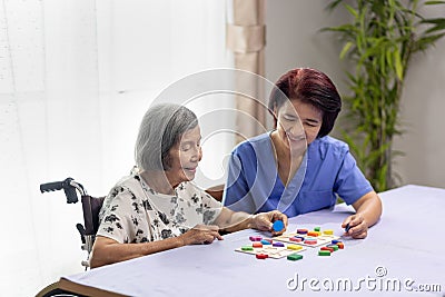 Caregiver and senior woman playing wooden shape puzzles game for dementia prevention Stock Photo