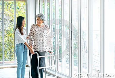 Caregiver, smiling young Asian female, daughter or grandchild supporting help elderly woman, mother or grandparents try to walk. Stock Photo