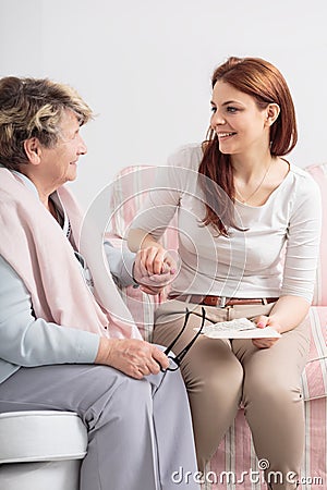 Caregiver talking with smiling senior woman while visit her at nursing house Stock Photo