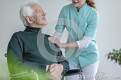 Caregiver talking to a happy man in a wheelchair in a nursing ho Stock Photo