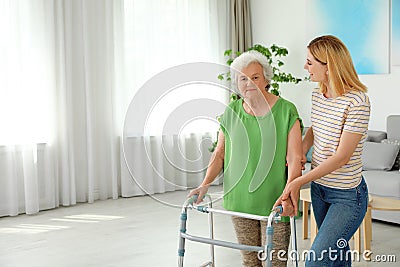 Caretaker helping elderly with walking frame indoors Stock Photo