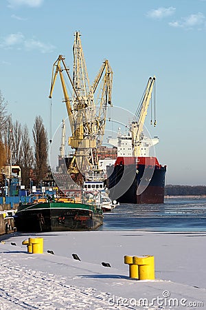 Cargo ship on harbor. Port crane and mooring bollards on a pier by frozen Odra River in Szczecin, Poland Editorial Stock Photo