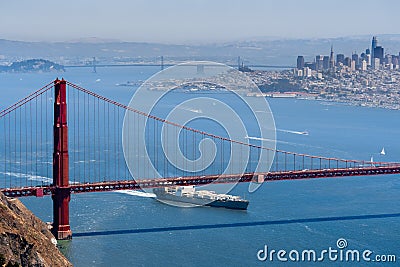 Cargo ship passing under Golden Gate Bridge on a sunny day; San Francisco skyline in the background; California Stock Photo