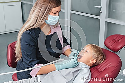 Caries treatment procedure in stomatology clinic close-up. Dentist in uniform holding dental tools. Young boy sitting in the chair Stock Photo