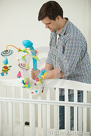 Caring father assembling baby`s cot and putting toy carousel in Stock Photo