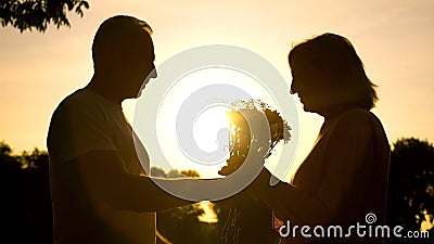 Caring man presenting flowers to woman at sunset, wedding anniversary, love Stock Photo