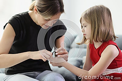 Caring mommy cuts off nails of daughter sitting on sofa Stock Photo