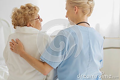 Volunteer sitting on a hospice bed next to an senior resident and strokes her back Stock Photo