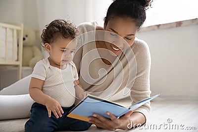 Caring young african woman reading fairy tale story to baby. Stock Photo