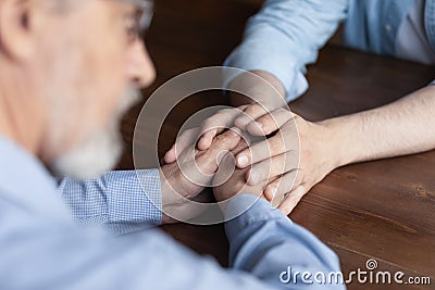 Caring young man adult child hold old man parent hands Stock Photo