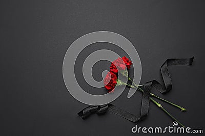 Black funeral ribbon with carnation flowers on dark background Stock Photo