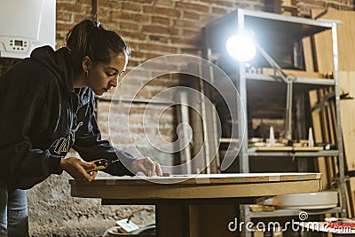 Carpenter / Artisan girl is concentrated working on an old wood table in her workshop. Woman restores an antique furniture Stock Photo