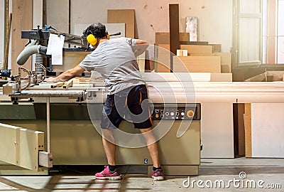 Carpenter cutting wood with a machine wearing earplugs Editorial Stock Photo