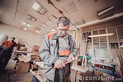 Carpenter handyman sharpening pencil with pocket knife on woodwork workshop table. Stock Photo