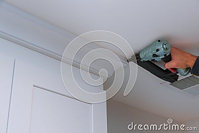 Carpenter nailing crown moldings in the kitchen cabinets framing trim worker using brad nail gun Stock Photo