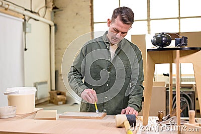 Carpenter paints wooden slat for production of furniture on table in workshop Stock Photo