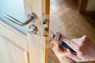 Carpenter repairing door lock. Installing a door handle. Handyman tightening door hinge . Hands of the repairman with a Stock Photo