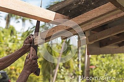 A carpenter saws off the excess edge of a wood rafter. Building or reconstructing a wooden roof frame for a rural home Stock Photo