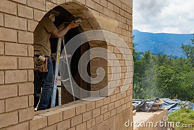 A carpenter on a step ladder grinding an adobe brick frame to accommodate a window Stock Photo