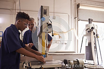 Carpenter Training Male Apprentice To Use Mechanized Saw Stock Photo