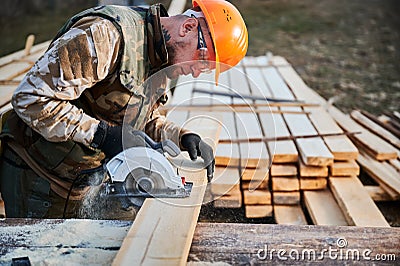 Carpenter using circular saw for cutting joist for building wooden frame house. Stock Photo