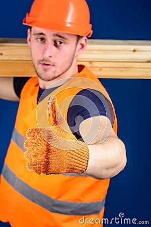 Carpenter, woodworker, builder on strict face carries wooden beam on shoulder. Wooden materials concept. Man in helmet Stock Photo