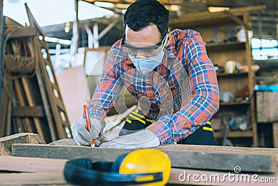 Carpenter is working in a woodworking office.caucasion white Carpenter using tape measure to measure distance and marking with Stock Photo