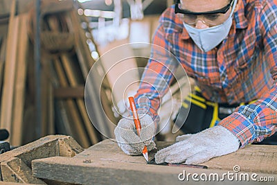 Carpenter is working in a woodworking office.caucasion white Carpenter using tape measure to measure distance and marking with Stock Photo