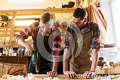 Carpenters with drill drilling plank at workshop Stock Photo