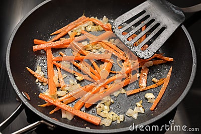 Carrot strips or julienne with onions and thyme are sauteed in a black frying pan, preparing vegetables for cooking a healthy Stock Photo