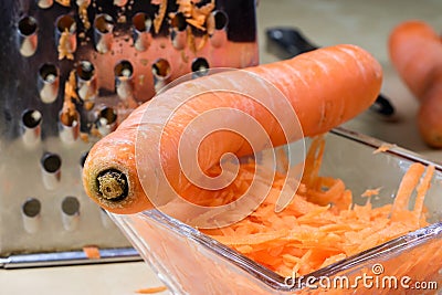 Carrots take off on a kitchen grater. Kitchen countertop and preparation of salads. Stock Photo